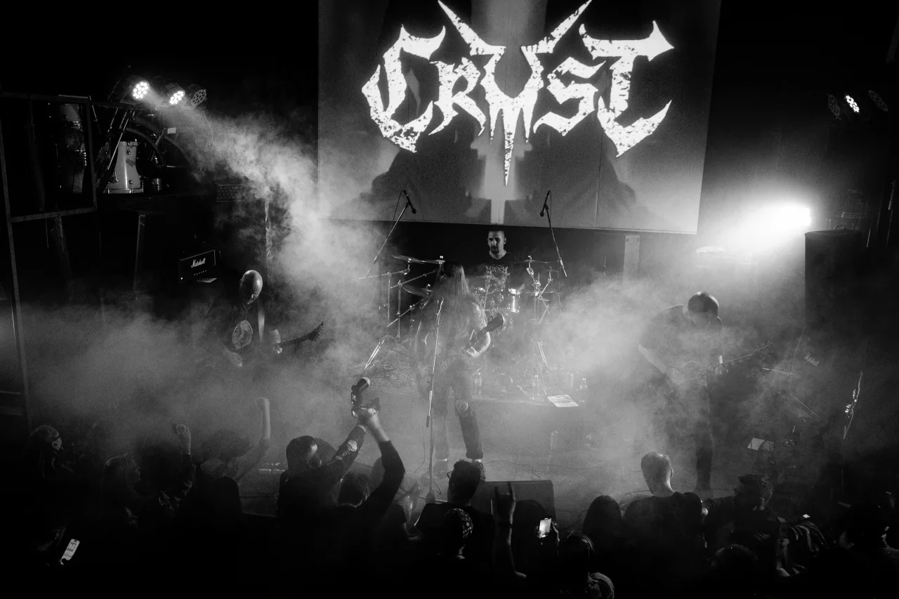 Группа Crust выступает на сцене перед зрителями; на экране виден логотип Crust.